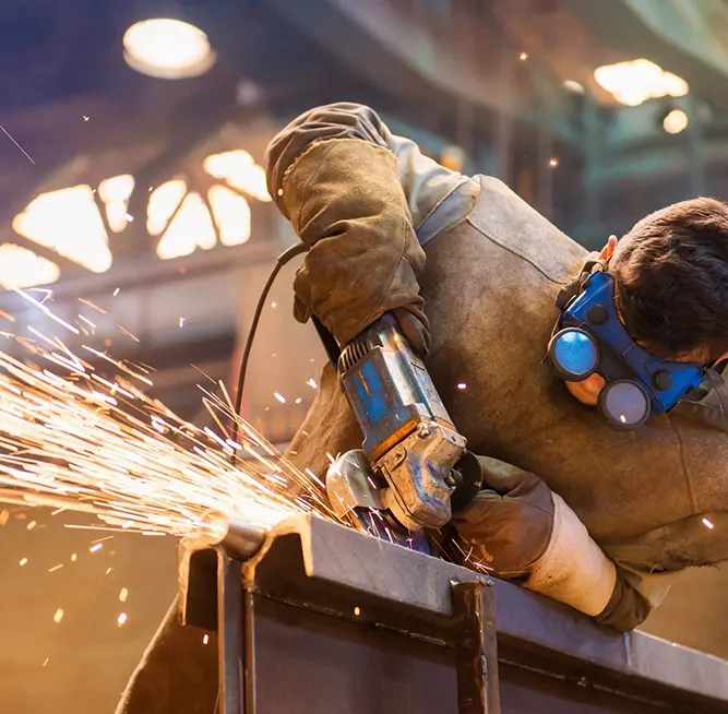 A man in protective gear using an angle grinder.